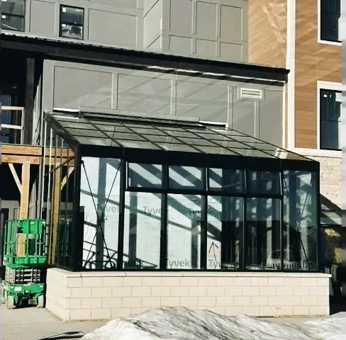 Glass sunroom addition with aluminum framing attached to a brick building